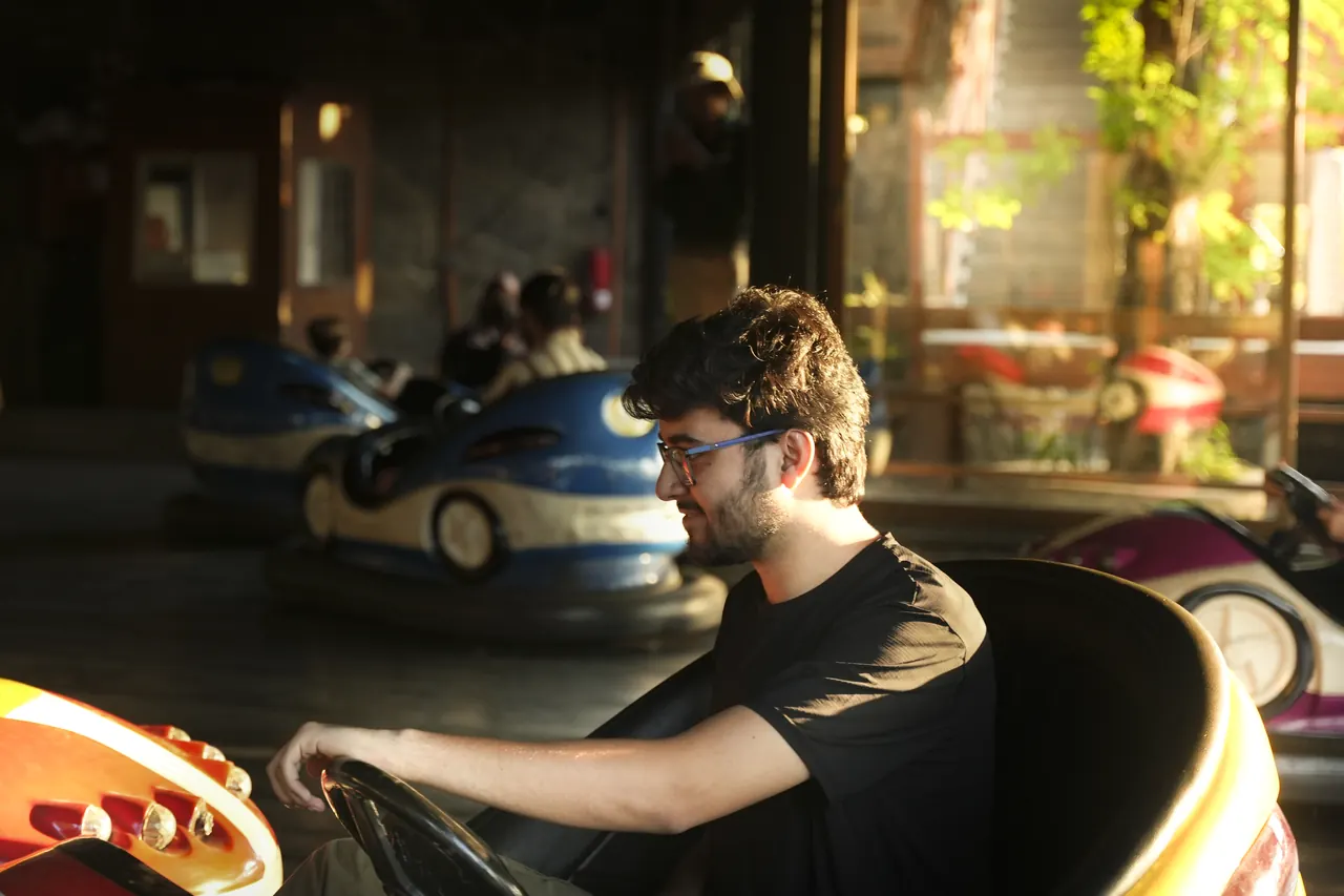A young man steering a bumper car under warm lights