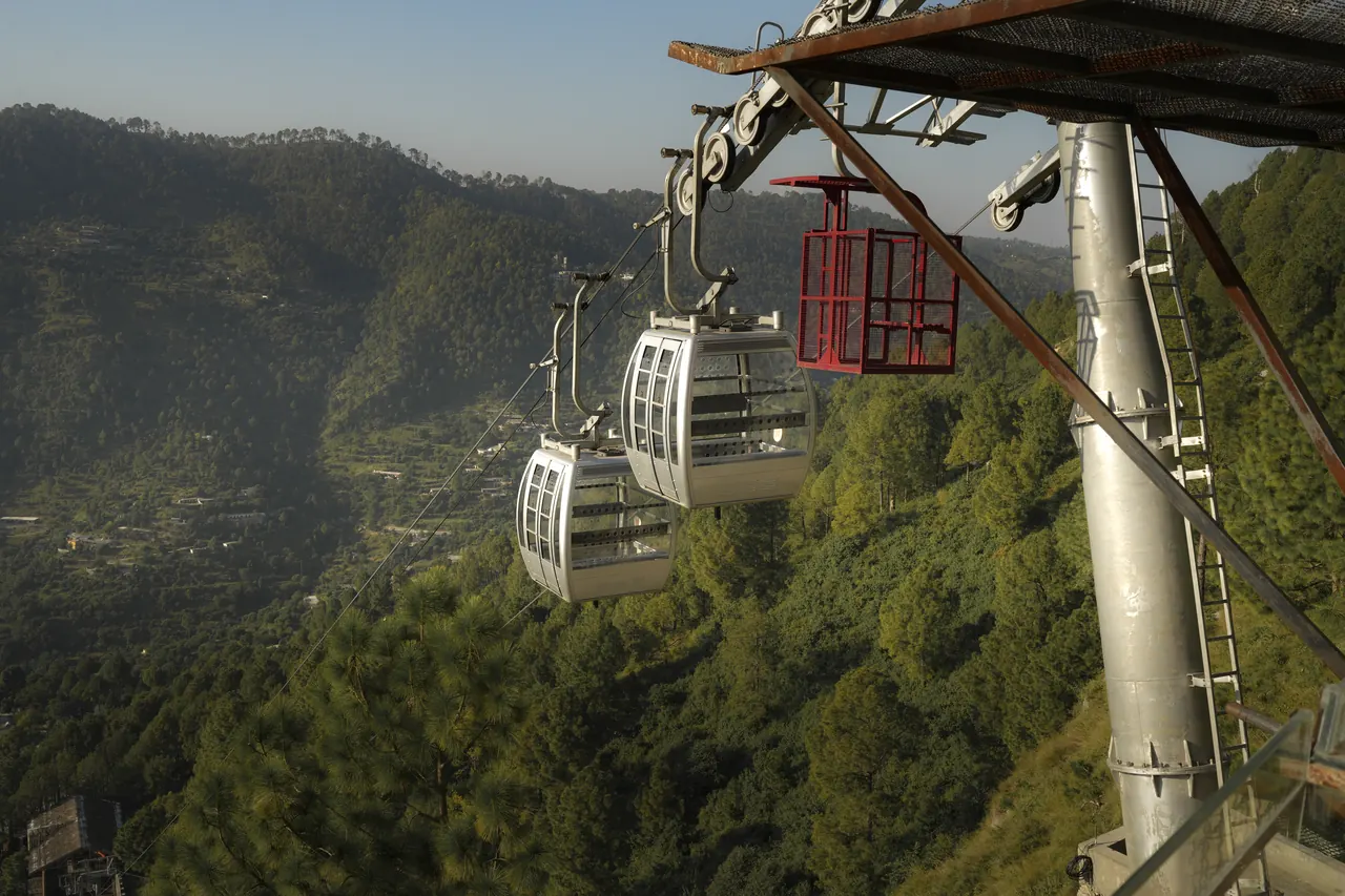 Two gondolas leaving the station tower above a forested valley