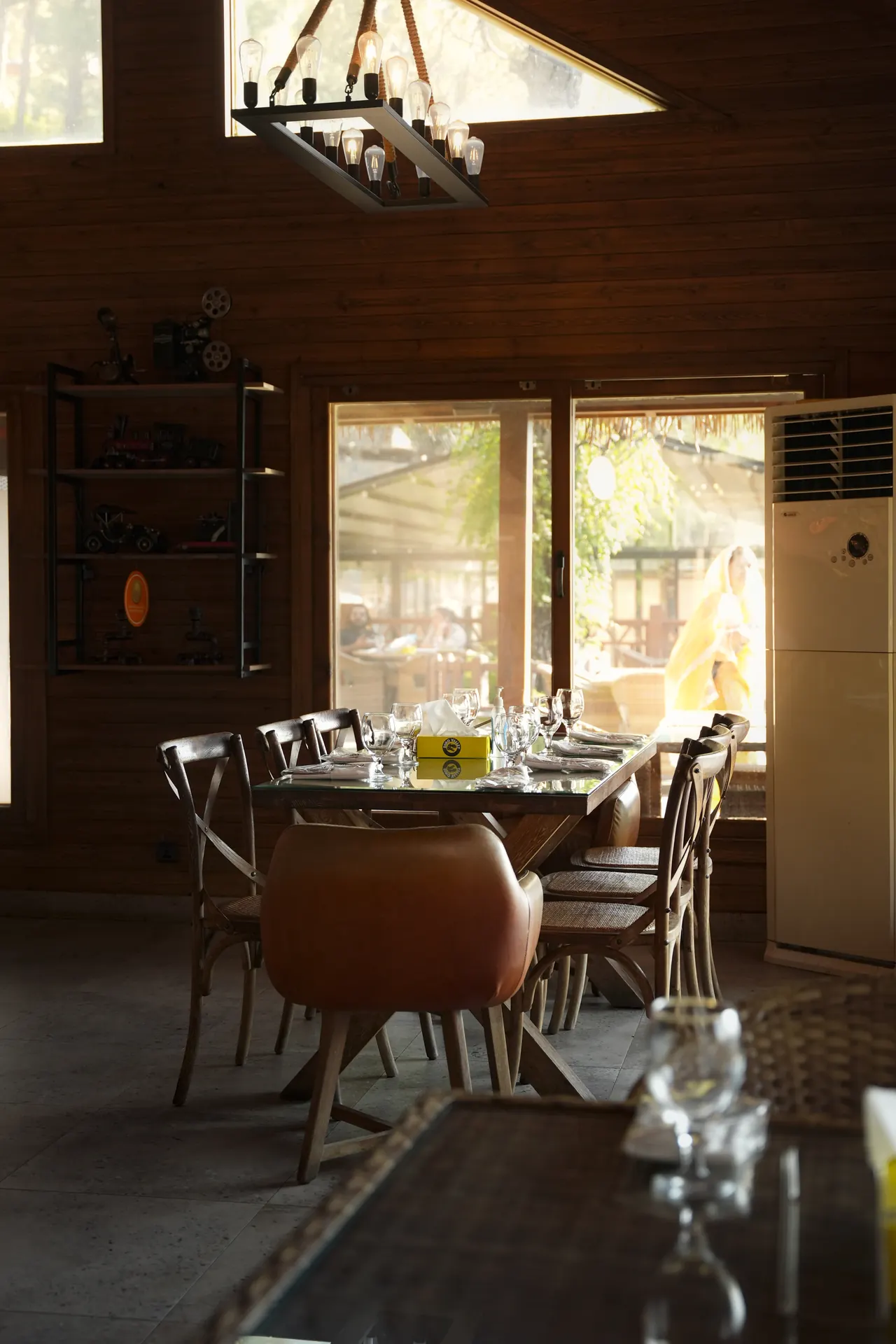 A dining room with timber walls and set tables by large windows