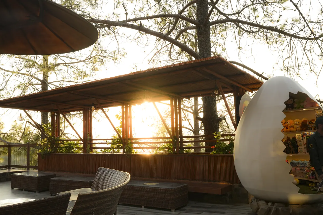 A giant cracked dinosaur egg kiosk on a deck at sunset