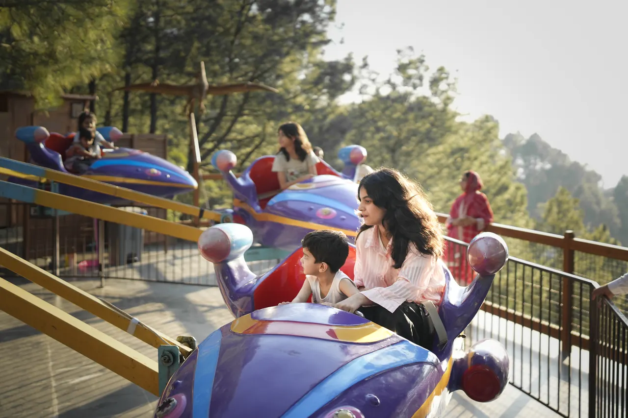 A mother and child laughing in a spinning spaceship ride on a hillside deck