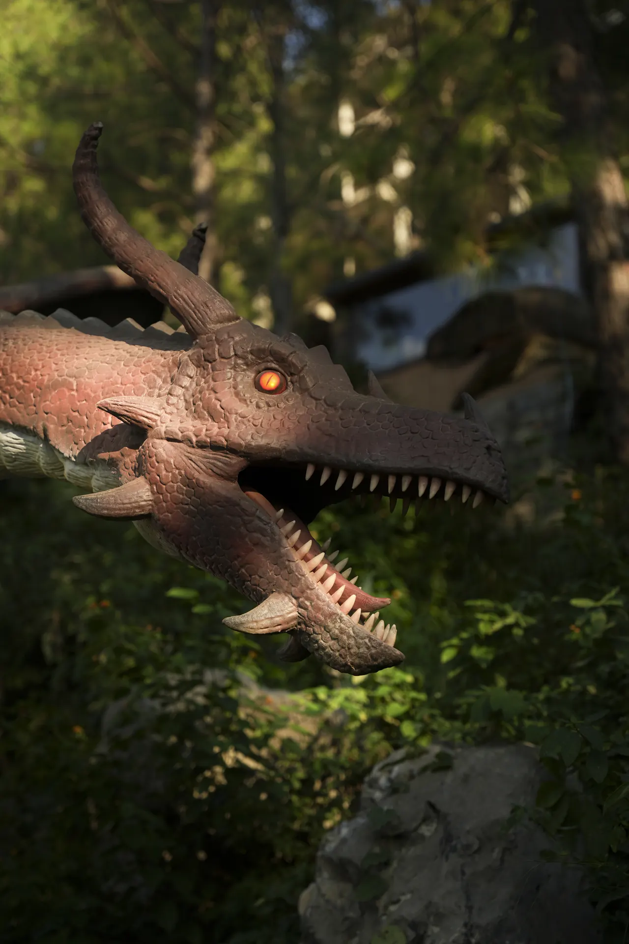 A horned dinosaur head with glowing eyes emerging from the forest
