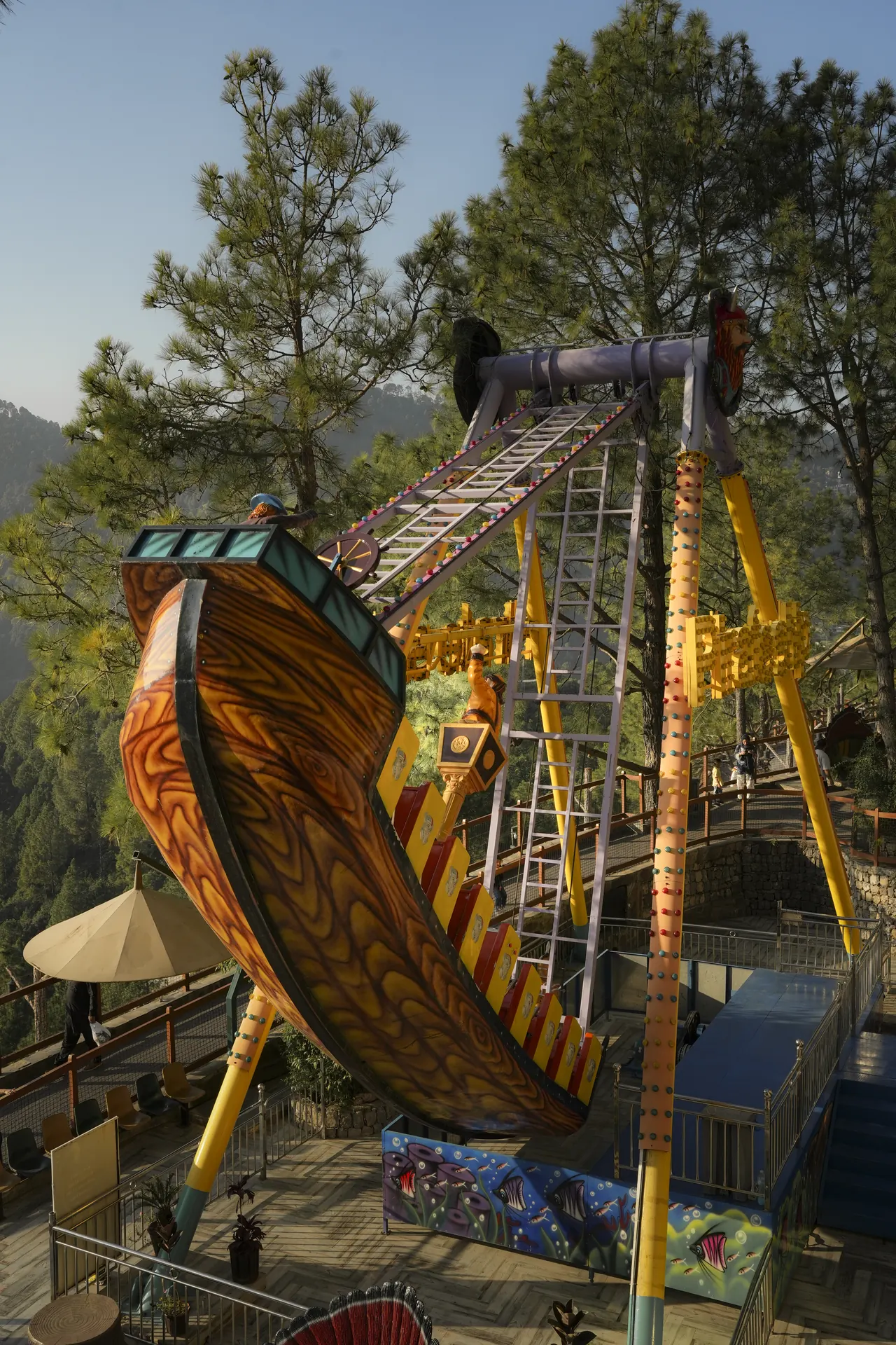A pirate ship swing ride at full height among pine trees